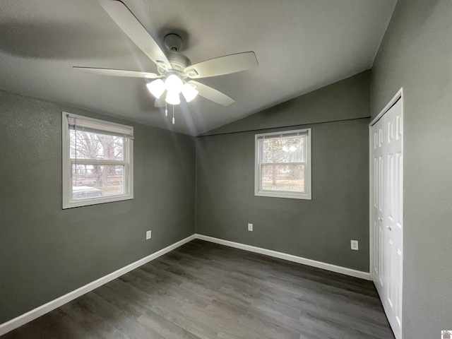 empty room with ceiling fan, a healthy amount of sunlight, dark hardwood / wood-style flooring, and vaulted ceiling