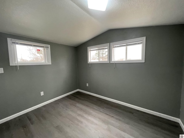 additional living space featuring hardwood / wood-style flooring, vaulted ceiling, and a textured ceiling