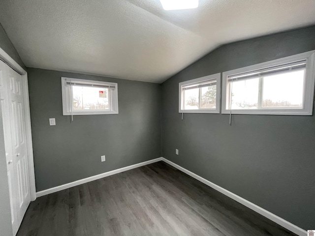 unfurnished room featuring vaulted ceiling, plenty of natural light, dark hardwood / wood-style floors, and a textured ceiling