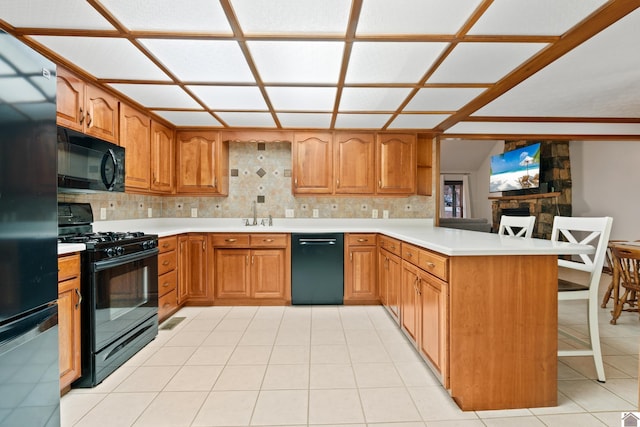 kitchen with light tile patterned floors, a kitchen breakfast bar, tasteful backsplash, black appliances, and kitchen peninsula