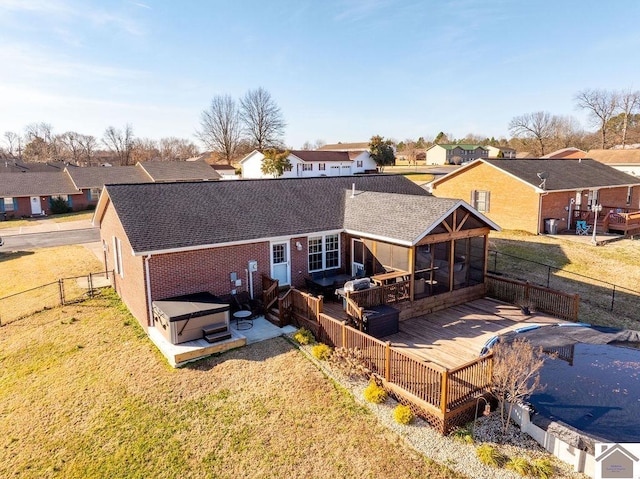 back of property featuring a hot tub, a sunroom, a deck, and a lawn