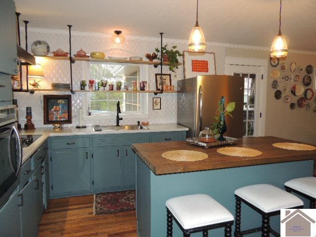 kitchen featuring blue cabinetry, sink, decorative light fixtures, stainless steel refrigerator, and ornamental molding