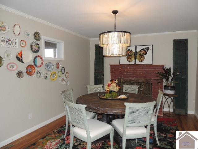 dining space featuring a notable chandelier, crown molding, wood-type flooring, and a brick fireplace