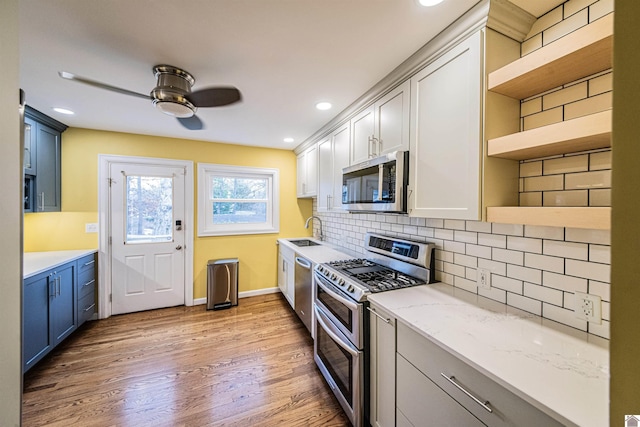 kitchen featuring sink, light hardwood / wood-style flooring, blue cabinetry, appliances with stainless steel finishes, and tasteful backsplash