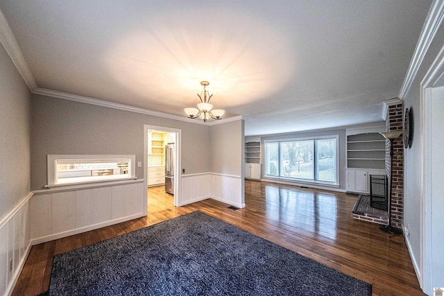 unfurnished living room featuring wood-type flooring, a notable chandelier, crown molding, and built in shelves