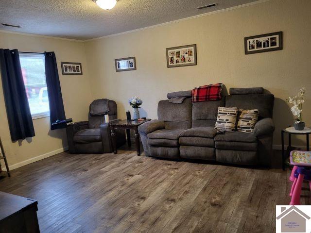 living area with visible vents, crown molding, a textured ceiling, and wood finished floors