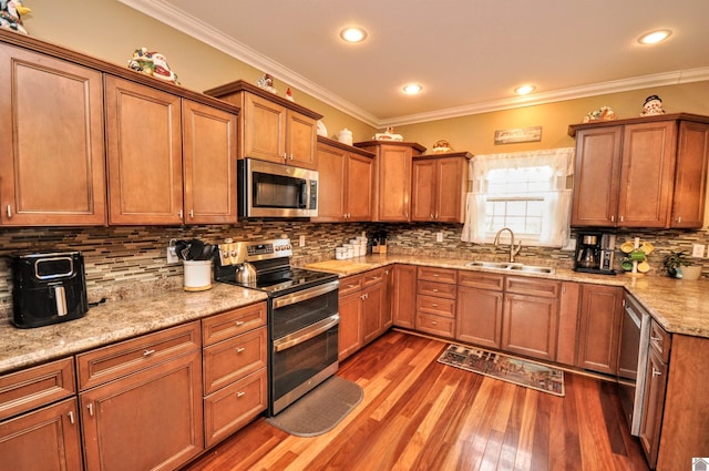 kitchen featuring sink, dark wood-type flooring, appliances with stainless steel finishes, ornamental molding, and light stone countertops