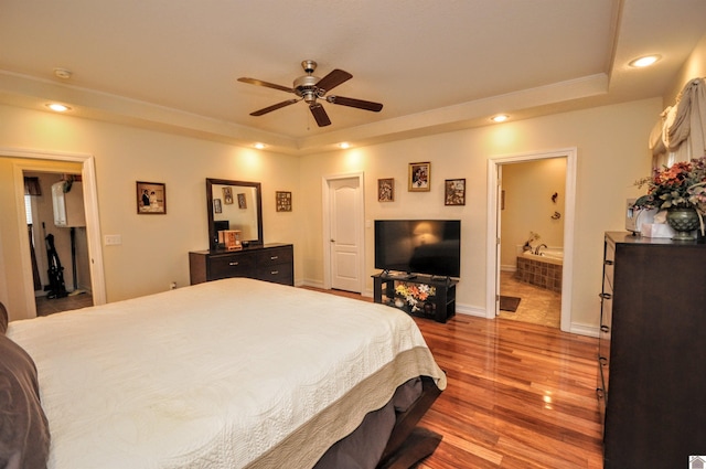 bedroom with ensuite bathroom, hardwood / wood-style floors, ceiling fan, and a tray ceiling