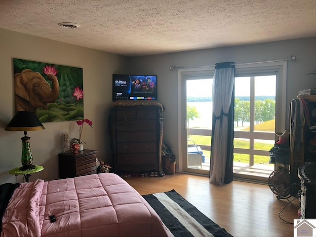 bedroom featuring access to exterior, light hardwood / wood-style flooring, and a textured ceiling