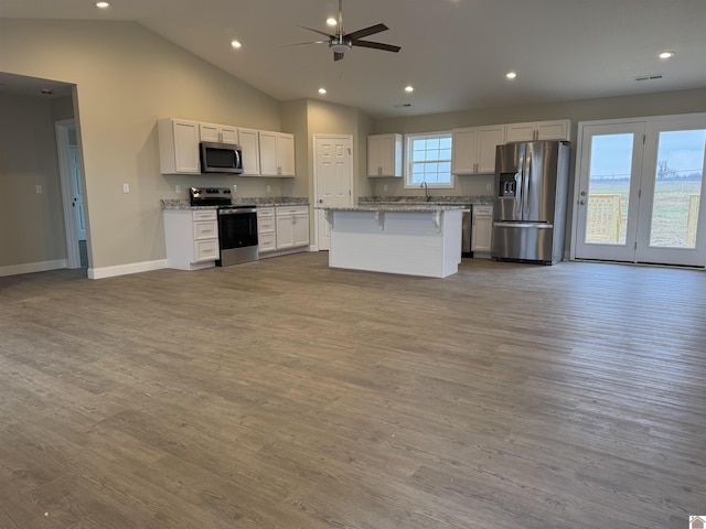 kitchen featuring light stone countertops, stainless steel appliances, a center island, and white cabinets