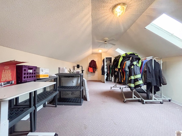 interior space with ceiling fan, lofted ceiling with skylight, a textured ceiling, and carpet