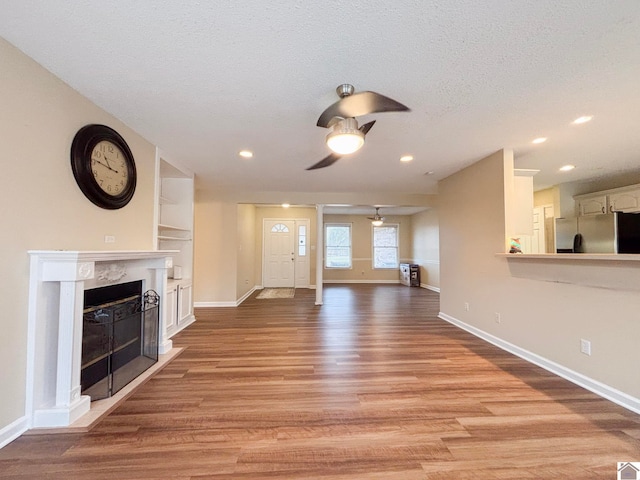 unfurnished living room featuring ceiling fan, a high end fireplace, light hardwood / wood-style floors, a textured ceiling, and built in shelves