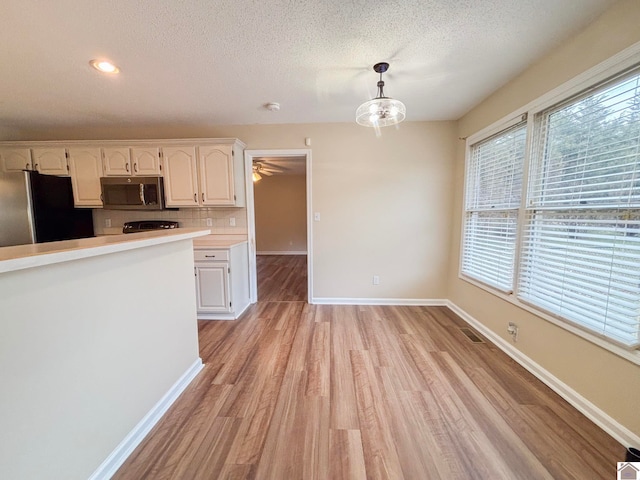 kitchen with pendant lighting, tasteful backsplash, white cabinets, stainless steel appliances, and light wood-type flooring