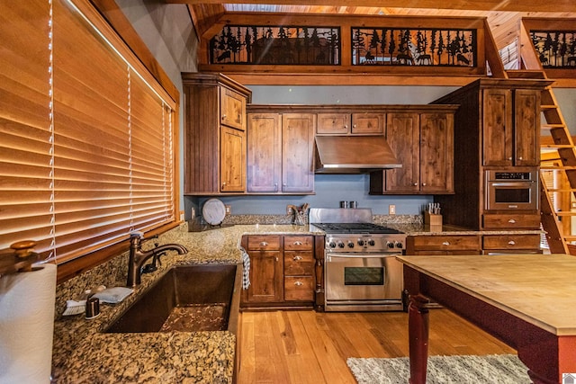 kitchen with extractor fan, sink, light hardwood / wood-style floors, stainless steel appliances, and light stone countertops