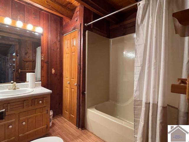 full bathroom featuring wood walls, vanity, shower / bathtub combination with curtain, beam ceiling, and hardwood / wood-style floors