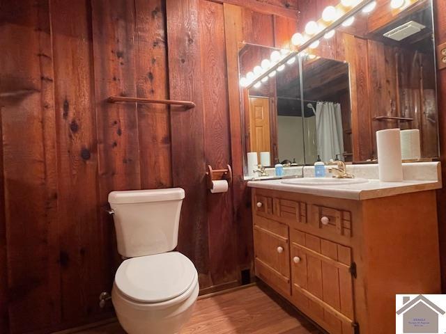 bathroom featuring toilet, vanity, wooden walls, and wood-type flooring