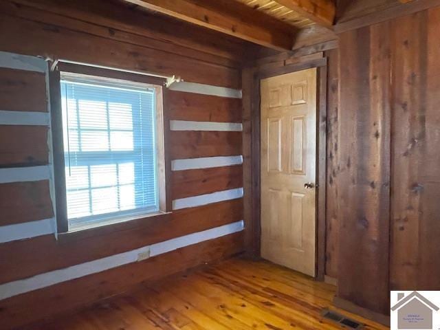 hallway with hardwood / wood-style flooring, wooden walls, and beam ceiling