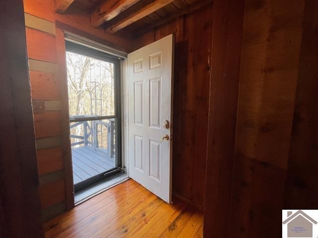 doorway to outside featuring beam ceiling, light hardwood / wood-style flooring, and wood walls