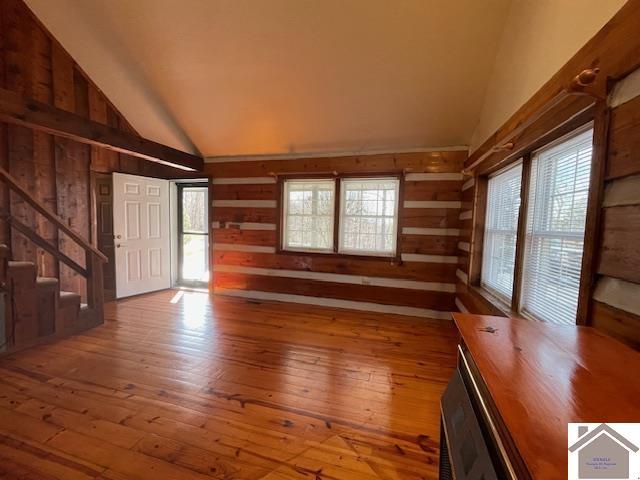 unfurnished living room featuring wood-type flooring, high vaulted ceiling, and wood walls