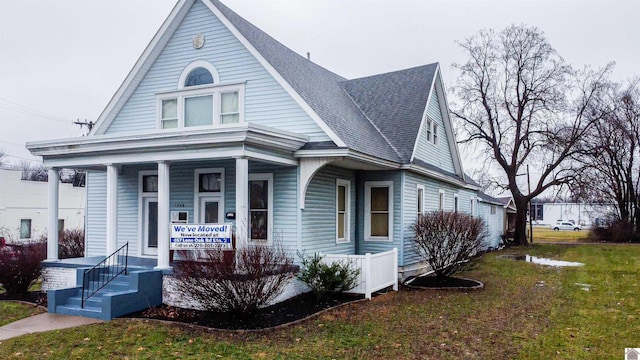 bungalow with a shingled roof, covered porch, and a front yard