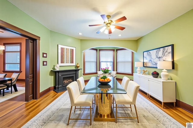 dining space featuring light wood finished floors, baseboards, a ceiling fan, and a fireplace with raised hearth