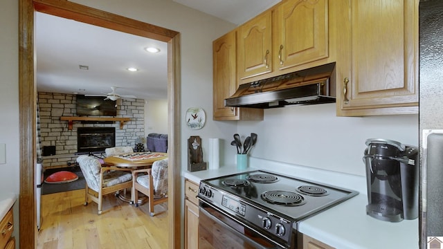 kitchen with light brown cabinetry, black electric range oven, ceiling fan, a brick fireplace, and light hardwood / wood-style flooring