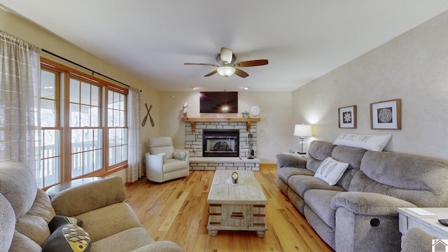 living room featuring ceiling fan, a stone fireplace, and light hardwood / wood-style floors