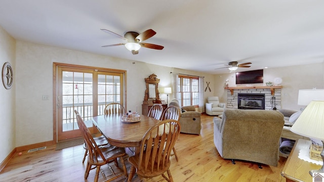 dining area with ceiling fan, a stone fireplace, and light hardwood / wood-style flooring