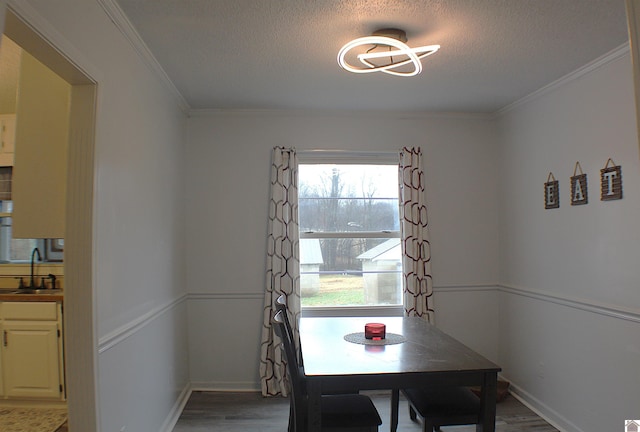 dining space with hardwood / wood-style flooring, crown molding, sink, and a textured ceiling