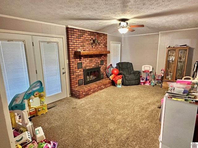 recreation room with a fireplace, carpet flooring, ornamental molding, ceiling fan, and a textured ceiling