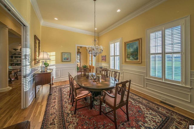 dining room featuring an inviting chandelier, crown molding, wood-type flooring, and decorative columns