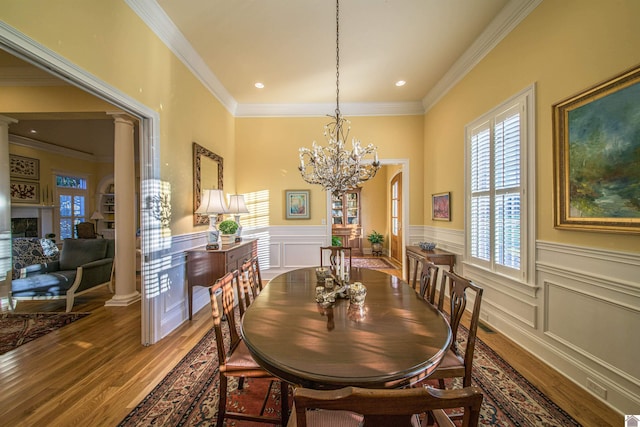 dining space featuring hardwood / wood-style flooring, crown molding, an inviting chandelier, and ornate columns