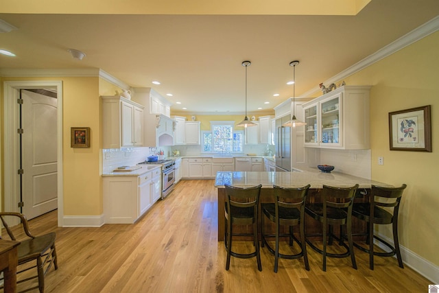 kitchen with white cabinetry, a kitchen breakfast bar, high end stainless steel range oven, kitchen peninsula, and crown molding