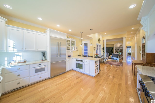 kitchen featuring built in fridge, decorative columns, white cabinets, hanging light fixtures, and kitchen peninsula