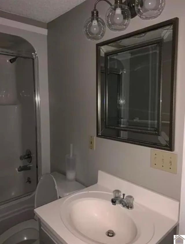 full bathroom featuring vanity, bath / shower combo with glass door, toilet, and a textured ceiling