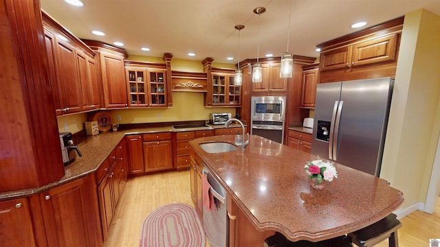 kitchen with a kitchen island with sink, hanging light fixtures, sink, dark stone counters, and appliances with stainless steel finishes