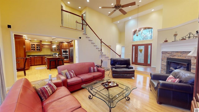 living room featuring a high ceiling, light wood-type flooring, a stone fireplace, ceiling fan with notable chandelier, and sink