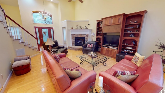 living room with ceiling fan with notable chandelier, light hardwood / wood-style flooring, a fireplace, and a towering ceiling