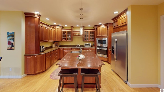 kitchen featuring appliances with stainless steel finishes, a center island with sink, hanging light fixtures, a breakfast bar area, and sink