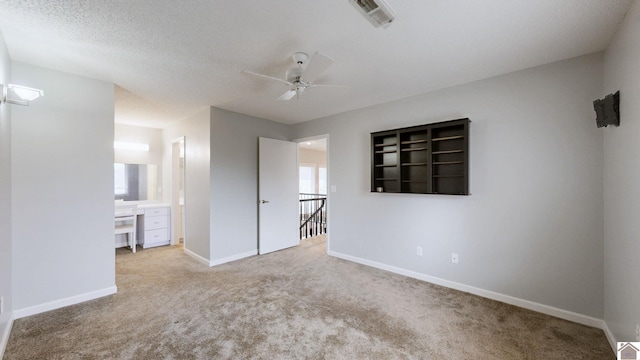 unfurnished bedroom featuring light carpet, ceiling fan, connected bathroom, and a textured ceiling