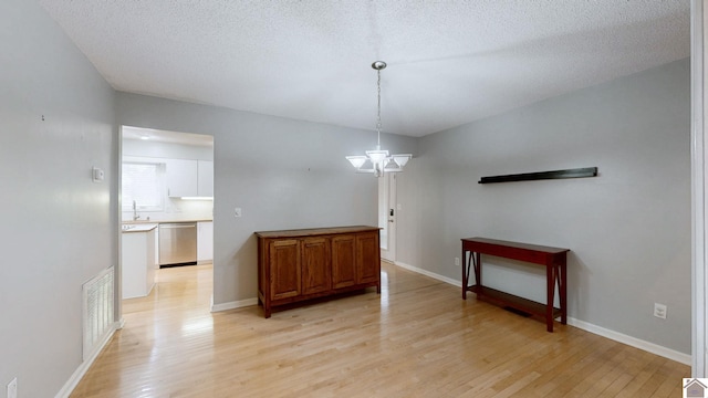 unfurnished dining area featuring sink, an inviting chandelier, a textured ceiling, and light hardwood / wood-style floors