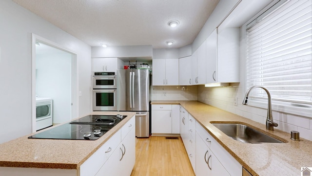 kitchen with sink, white cabinetry, appliances with stainless steel finishes, washer / clothes dryer, and light hardwood / wood-style floors