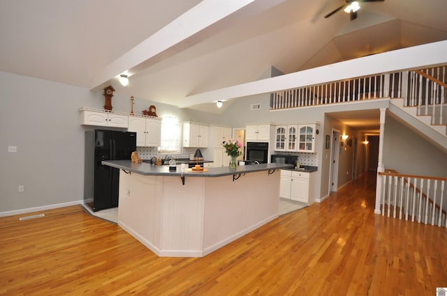 kitchen with light wood-type flooring, a kitchen bar, black appliances, and white cabinets