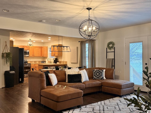 living room featuring sink, a textured ceiling, an inviting chandelier, and dark hardwood / wood-style flooring