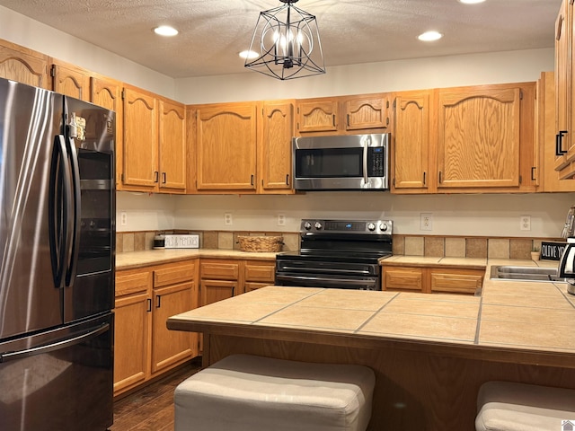 kitchen with stainless steel appliances, decorative light fixtures, sink, a textured ceiling, and dark wood-type flooring