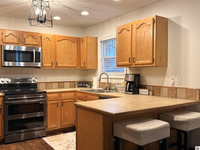 kitchen featuring stainless steel appliances, a textured ceiling, decorative light fixtures, sink, and kitchen peninsula