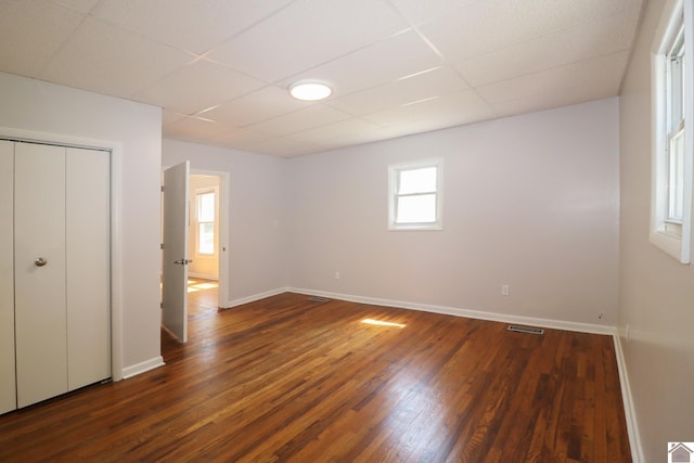 unfurnished bedroom with dark hardwood / wood-style flooring, a paneled ceiling, and a closet