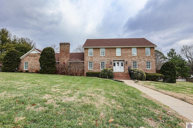 colonial-style house with brick siding, a chimney, and a front yard