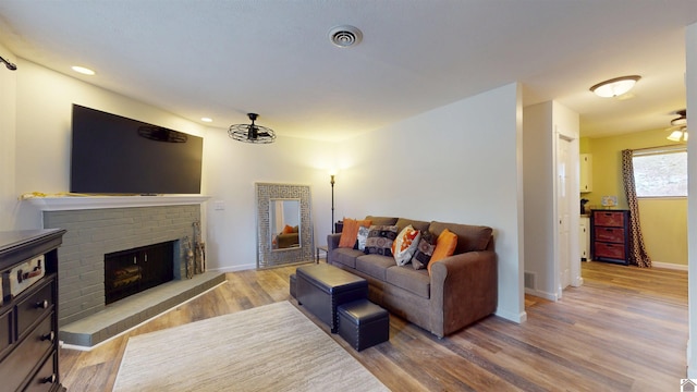 living area featuring recessed lighting, visible vents, light wood-style floors, a brick fireplace, and baseboards