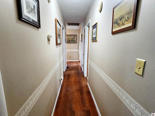 hallway featuring dark wood-style flooring, visible vents, a textured ceiling, and baseboards